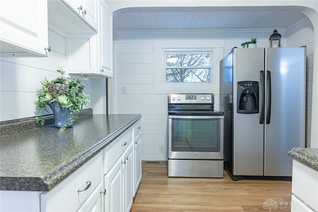 kitchen with light hardwood / wood-style flooring, stainless steel appliances, white cabinets, and wood walls