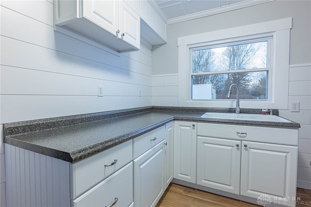 kitchen with white cabinetry, ornamental molding, sink, and wood-type flooring