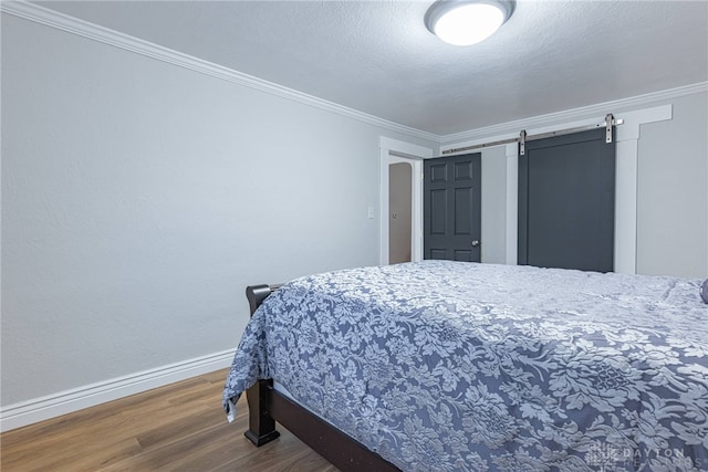 bedroom featuring crown molding, a barn door, hardwood / wood-style floors, and a textured ceiling