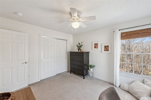 sitting room with a ceiling fan, baseboards, and light colored carpet