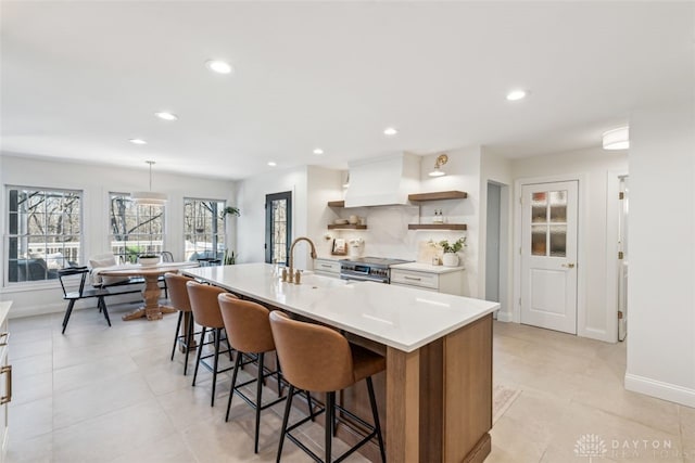 kitchen with open shelves, stainless steel stove, a kitchen breakfast bar, premium range hood, and a sink