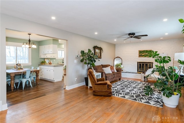 living room with sink, a brick fireplace, light wood-type flooring, brick wall, and ceiling fan with notable chandelier