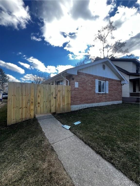 view of property exterior featuring fence, a lawn, and brick siding