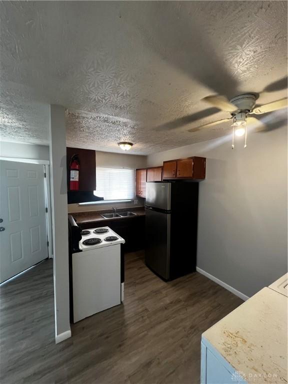 kitchen with white electric range oven, baseboards, dark wood finished floors, freestanding refrigerator, and a textured ceiling