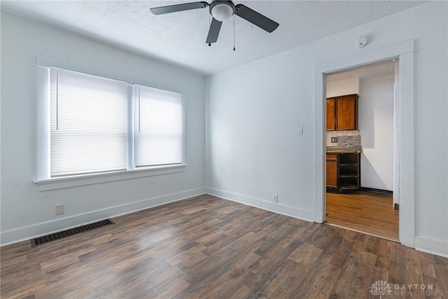 empty room with ceiling fan, dark wood-type flooring, and a textured ceiling