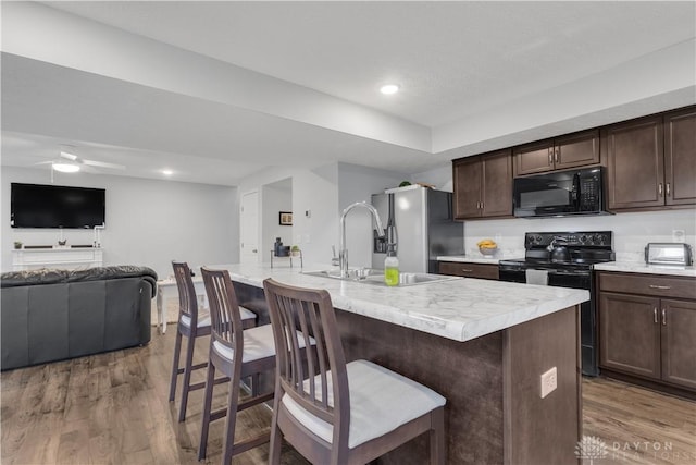 kitchen with hardwood / wood-style flooring, a center island with sink, a kitchen bar, and black appliances