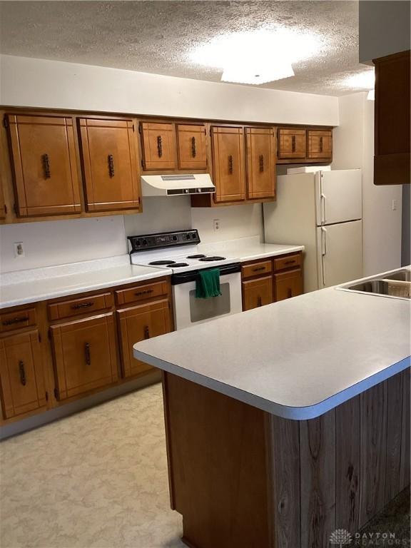 kitchen featuring white appliances, kitchen peninsula, sink, and a textured ceiling