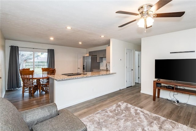 kitchen with dark wood-type flooring, gray cabinetry, stainless steel fridge with ice dispenser, kitchen peninsula, and light stone countertops