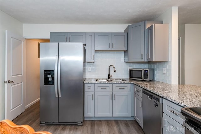 kitchen featuring sink, dark wood-type flooring, stainless steel appliances, light stone counters, and tasteful backsplash