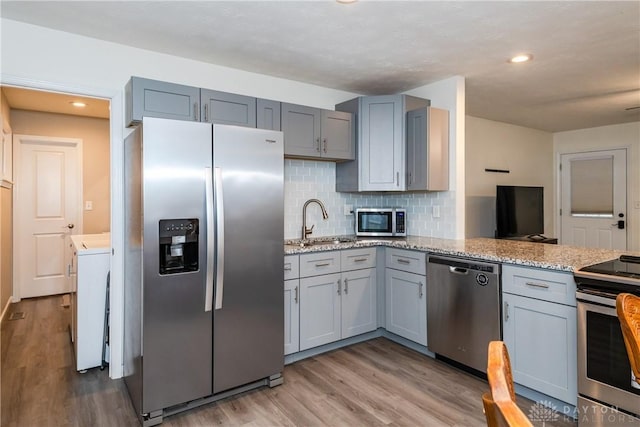 kitchen with washer / dryer, sink, light stone counters, stainless steel appliances, and light hardwood / wood-style flooring