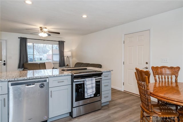 kitchen featuring ceiling fan, appliances with stainless steel finishes, light stone countertops, and light wood-type flooring