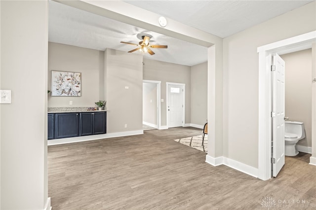 interior space with ceiling fan, light wood finished floors, a textured ceiling, and baseboards