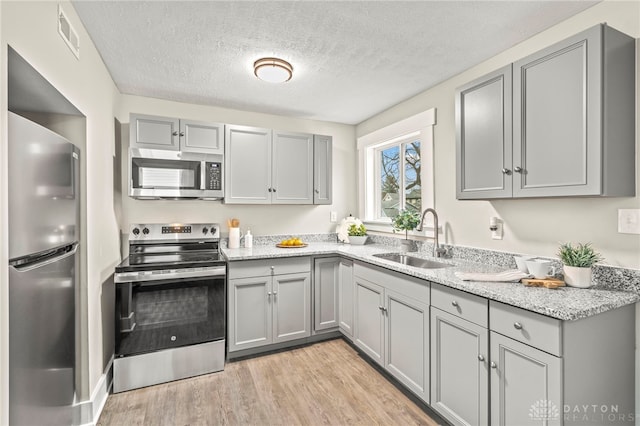 kitchen with appliances with stainless steel finishes, a sink, light wood finished floors, and light stone counters