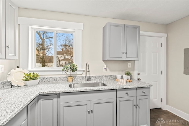 kitchen featuring baseboards, light stone counters, dark wood-type flooring, gray cabinets, and a sink