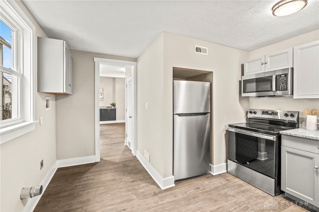 kitchen with baseboards, stainless steel appliances, a textured ceiling, light countertops, and light wood-type flooring