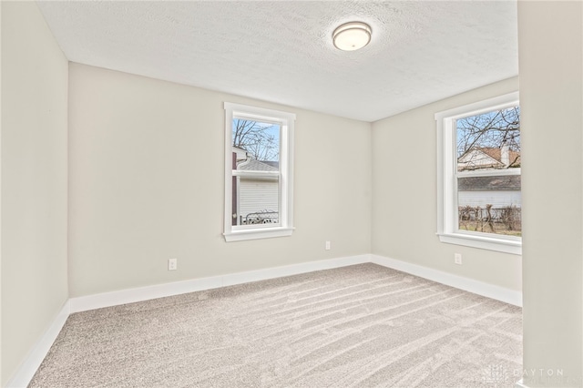 empty room with light colored carpet, a healthy amount of sunlight, a textured ceiling, and baseboards