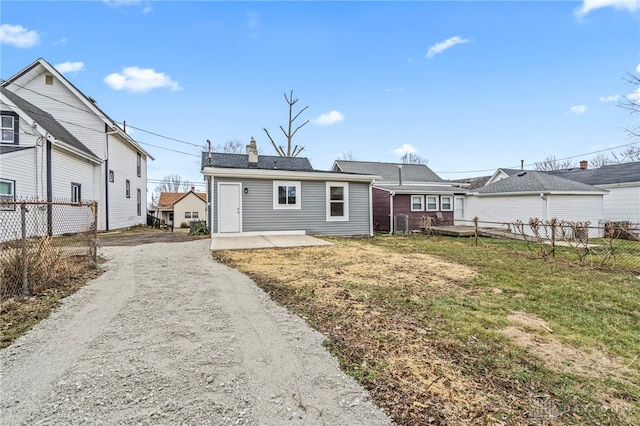 rear view of house featuring fence, driveway, a lawn, a chimney, and a patio area