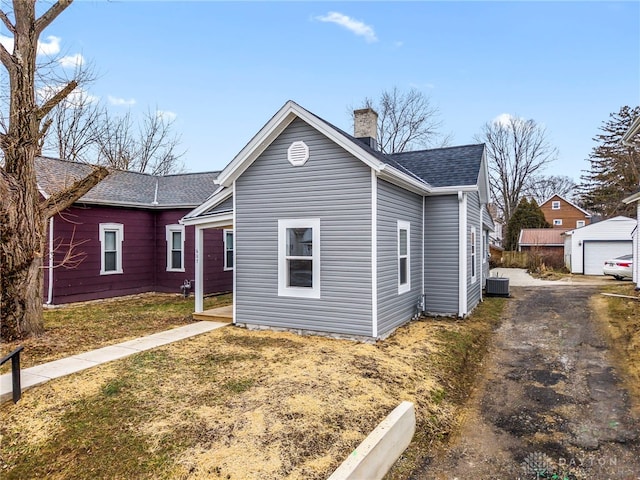 view of front of home with an outbuilding, central AC, a chimney, and roof with shingles