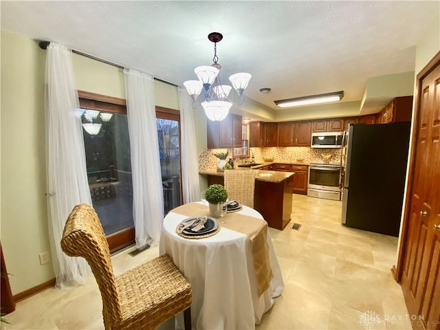 kitchen with pendant lighting, sink, stainless steel appliances, tasteful backsplash, and kitchen peninsula