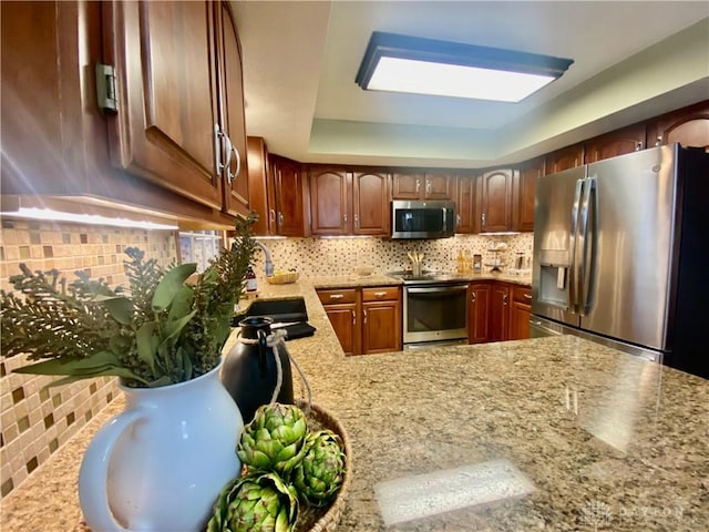 kitchen with tasteful backsplash, appliances with stainless steel finishes, a tray ceiling, and sink