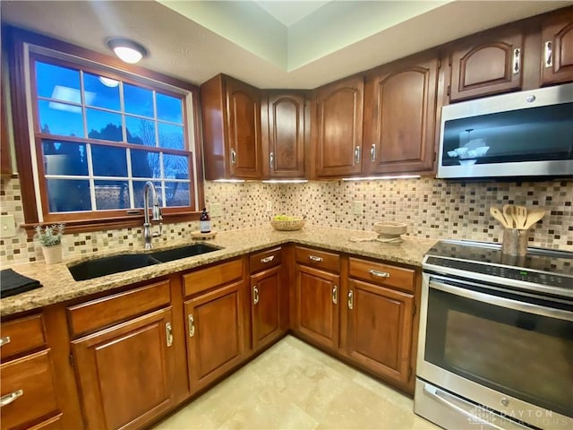 kitchen featuring light stone counters, sink, backsplash, and appliances with stainless steel finishes