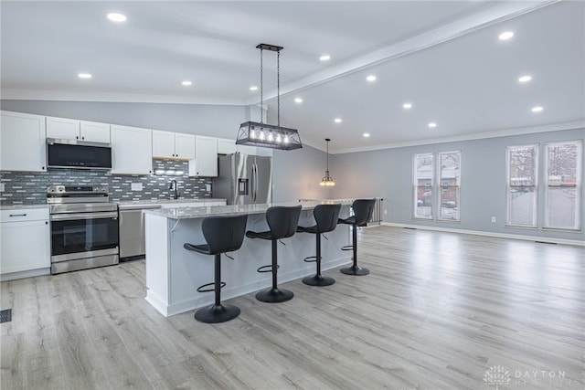 kitchen with appliances with stainless steel finishes, light wood finished floors, a center island, vaulted ceiling with beams, and tasteful backsplash