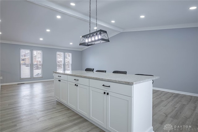 kitchen with a kitchen island, baseboards, lofted ceiling with beams, light wood finished floors, and ornamental molding