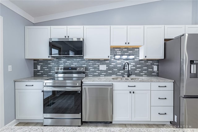 kitchen with appliances with stainless steel finishes, a sink, vaulted ceiling, and tasteful backsplash