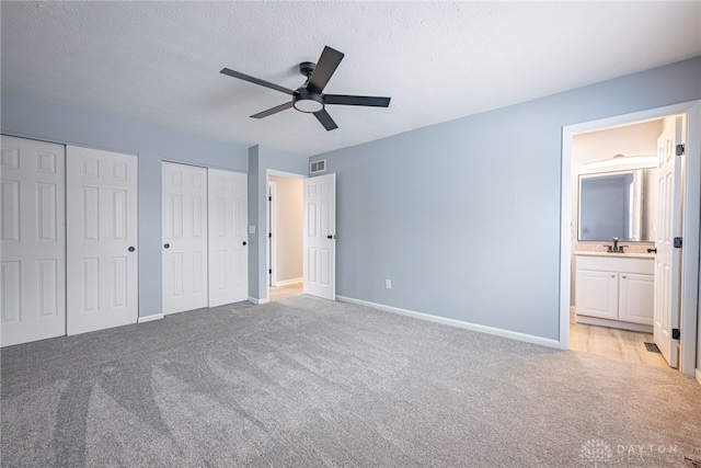 unfurnished bedroom featuring visible vents, baseboards, multiple closets, ensuite bathroom, and light carpet