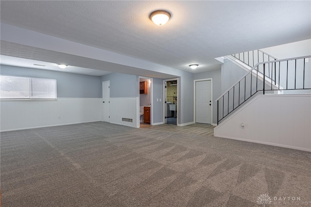 below grade area featuring carpet flooring, a textured ceiling, a wainscoted wall, stairs, and visible vents
