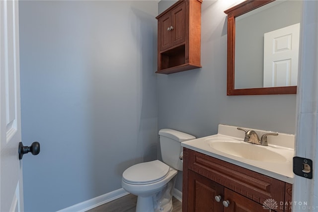 half bathroom with vanity, baseboards, and toilet