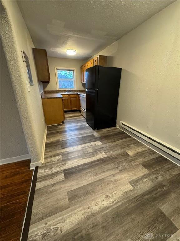 kitchen with a textured wall, stove, brown cabinets, dark wood-type flooring, and freestanding refrigerator