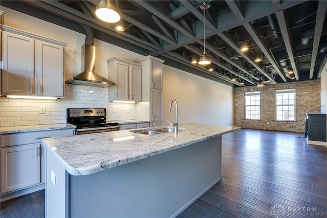 kitchen with light stone counters, sink, stainless steel electric stove, and wall chimney exhaust hood