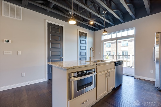 kitchen with sink, an island with sink, pendant lighting, stainless steel appliances, and light stone countertops