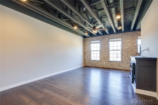 empty room with brick wall, dark wood-type flooring, and ceiling fan