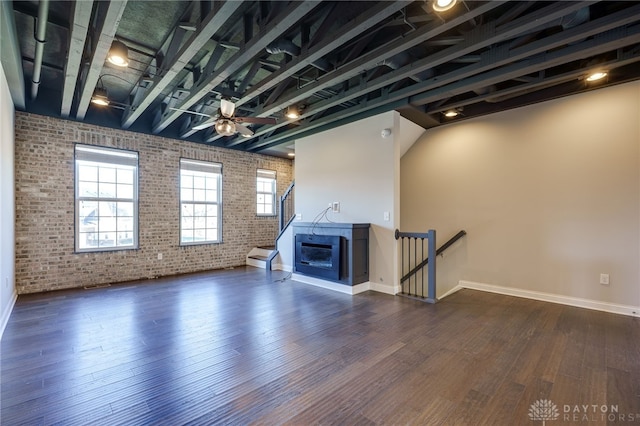 unfurnished living room with dark wood-type flooring, ceiling fan, and brick wall