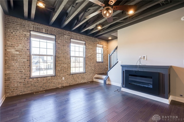 unfurnished living room featuring brick wall, dark hardwood / wood-style floors, beam ceiling, and plenty of natural light