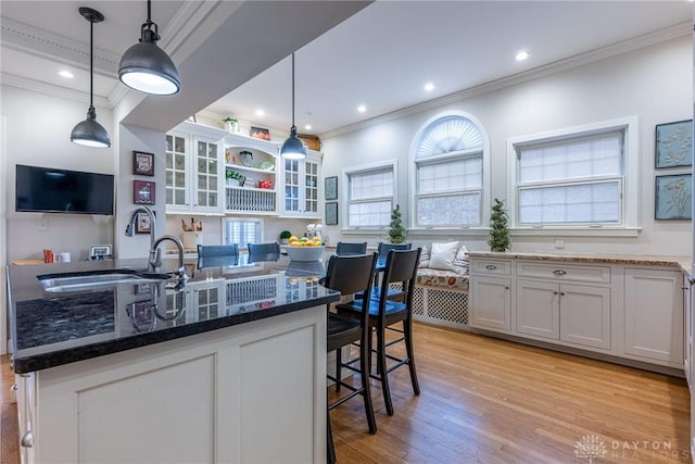 kitchen featuring white cabinetry, a kitchen bar, a kitchen island with sink, and hanging light fixtures