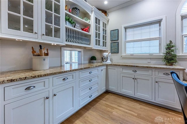 kitchen with white cabinetry, ornamental molding, light hardwood / wood-style flooring, and light stone countertops