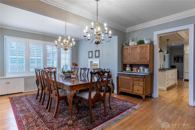 dining area featuring crown molding, sink, a chandelier, and light hardwood / wood-style floors