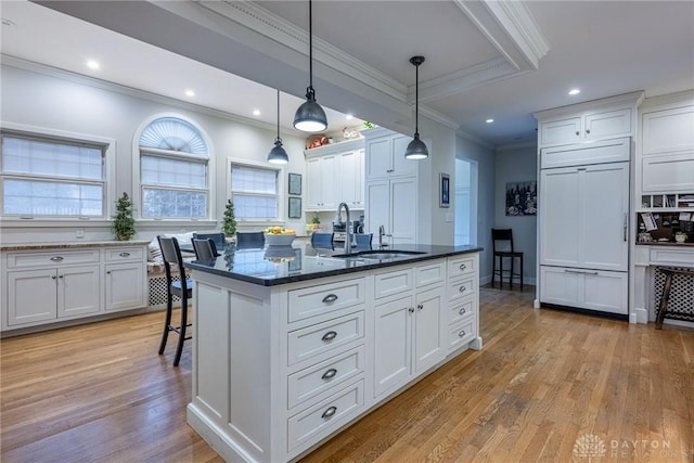 kitchen with pendant lighting, sink, paneled fridge, white cabinets, and a center island with sink