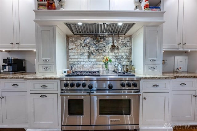 kitchen featuring premium range hood, range with two ovens, light stone countertops, decorative backsplash, and white cabinets