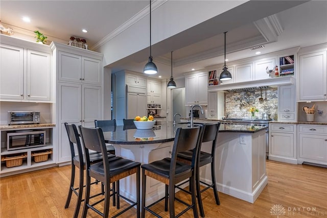 kitchen featuring white cabinetry, decorative light fixtures, a breakfast bar area, and an island with sink