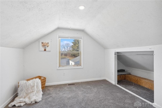 additional living space featuring baseboards, visible vents, vaulted ceiling, a textured ceiling, and carpet flooring