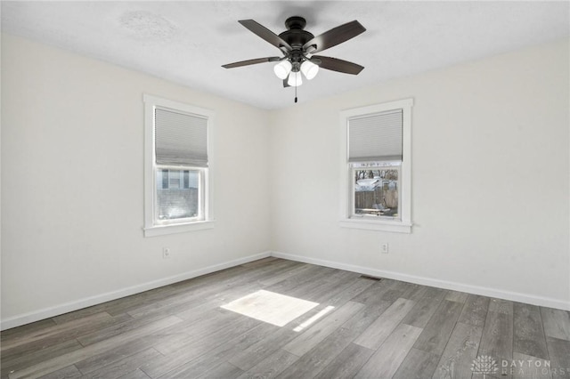 unfurnished room with visible vents, wood finished floors, a ceiling fan, and baseboards