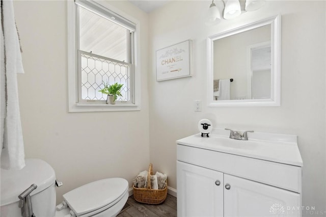 bathroom featuring toilet, baseboards, wood finished floors, and vanity