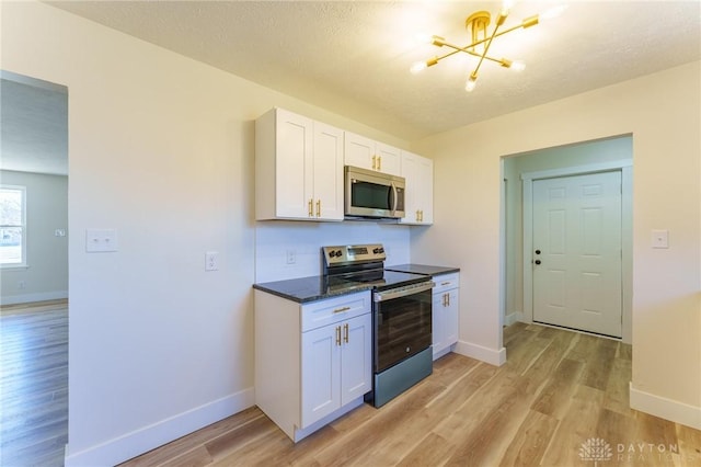 kitchen featuring appliances with stainless steel finishes, dark stone countertops, white cabinets, and light hardwood / wood-style floors