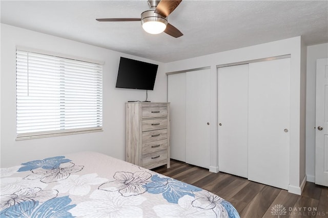 bedroom with multiple closets, dark hardwood / wood-style floors, a textured ceiling, and ceiling fan