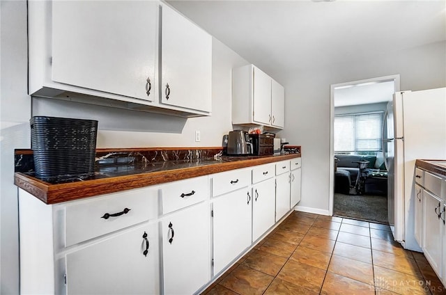 kitchen with dark countertops, freestanding refrigerator, white cabinetry, light tile patterned flooring, and baseboards