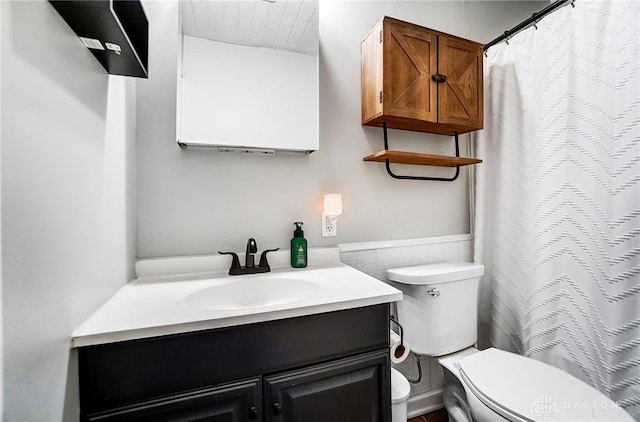 full bathroom featuring curtained shower, wainscoting, vanity, and toilet